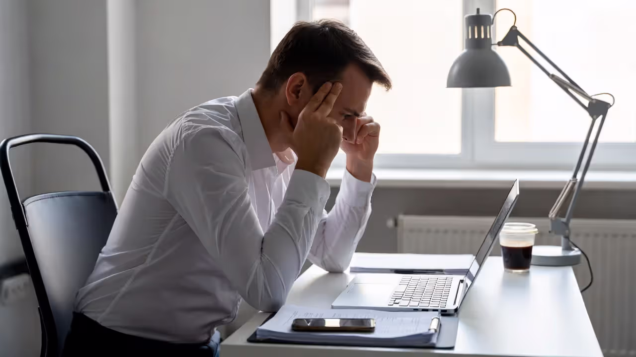 Stressed office employee sitting at desk with laptop and documents