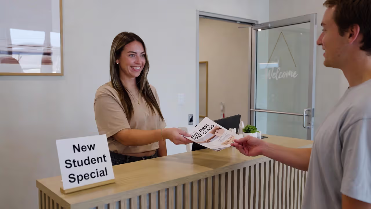 Studio staff member offering a free trial class brochure to a new student.