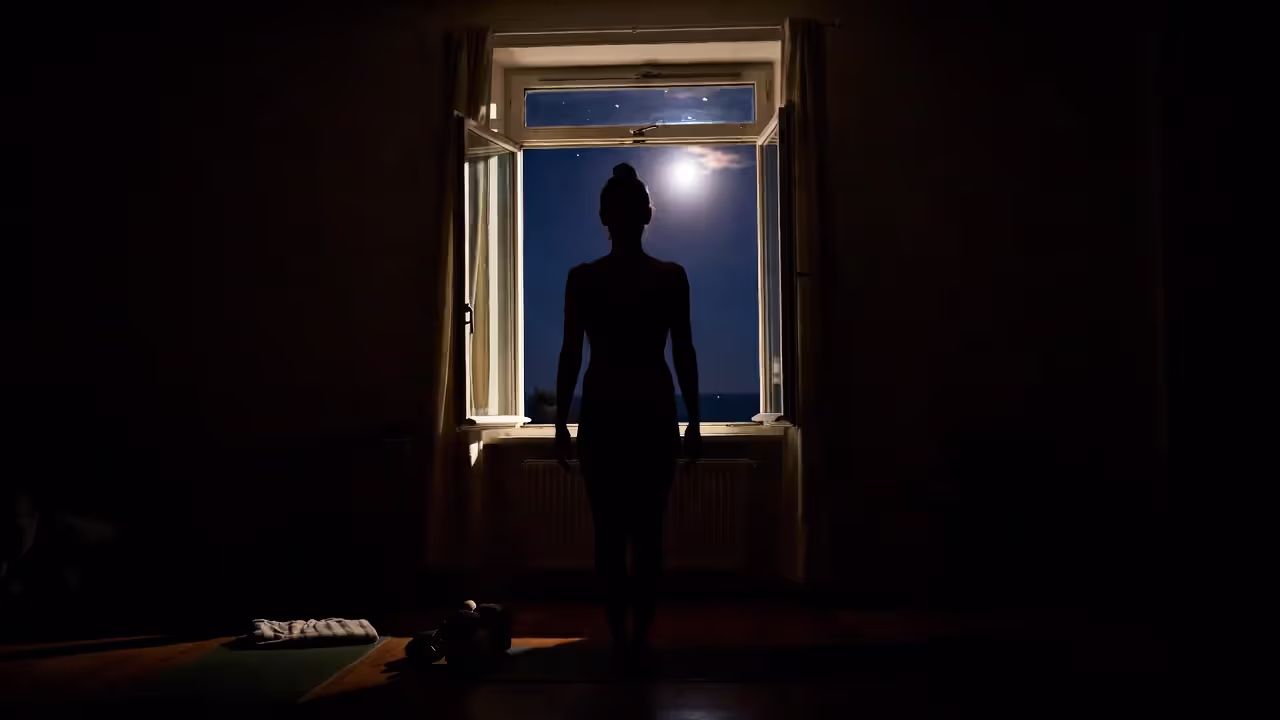 Person practicing yoga indoors near a window with the full moon visible outside.